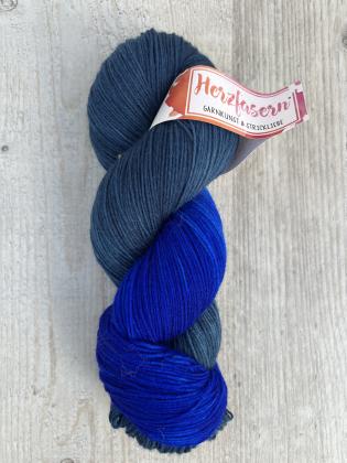 Handgefärbter Garnstrang Herzfasern No. 20 in der Farbe Tiefenblau. Dunkles Petrolgrau kombiniert mit kräftigem, leuchtendem Blau. Das Garn ist zu einem Strang gedreht und mit einer Herzfasern-Banderole versehen.